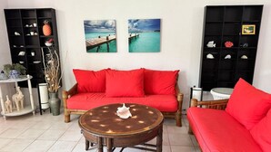 A living room with a red sofa, a round wooden coffee table, and two black shelves with decorative items. - Travelers Palm Beachy Paradise (Edgewater)