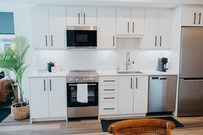 A modern kitchen with white cabinets, stainless steel appliances, and a herringbone-patterned backsplash. - Chic Downtown Condo Retreat (Kitchener)
