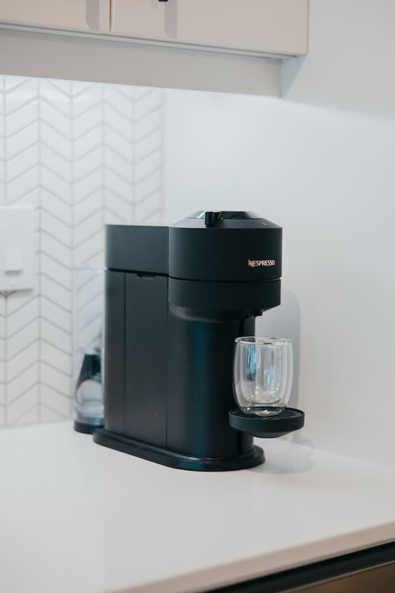 Une machine à café noire avec une tasse en verre posée sur le comptoir.