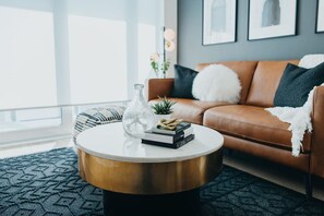A modern living room with a leather sofa, a round coffee table, and a large window. - Chic Downtown Condo Retreat (Kitchener)