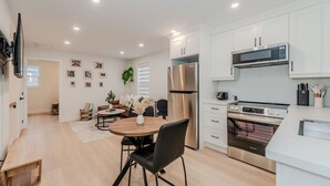 A modern kitchen with white cabinets, stainless steel appliances, and a dining area with a wooden table and black chairs. - Stylish 1BD Steps from Downtown (Kitchener)