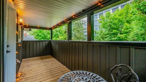 A covered outdoor area with a wooden deck, a metal table, and a metal chair. - Stylish 1BD Steps from Downtown (Kitchener)