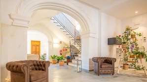Amplia sala de estar con un techo alto y un arco que da a una escalera. Hay dos sillones de cuero y una mesa de centro en el centro.