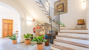 Una escalera con barandilla de hierro forjado, una puerta de madera y plantas en macetas.