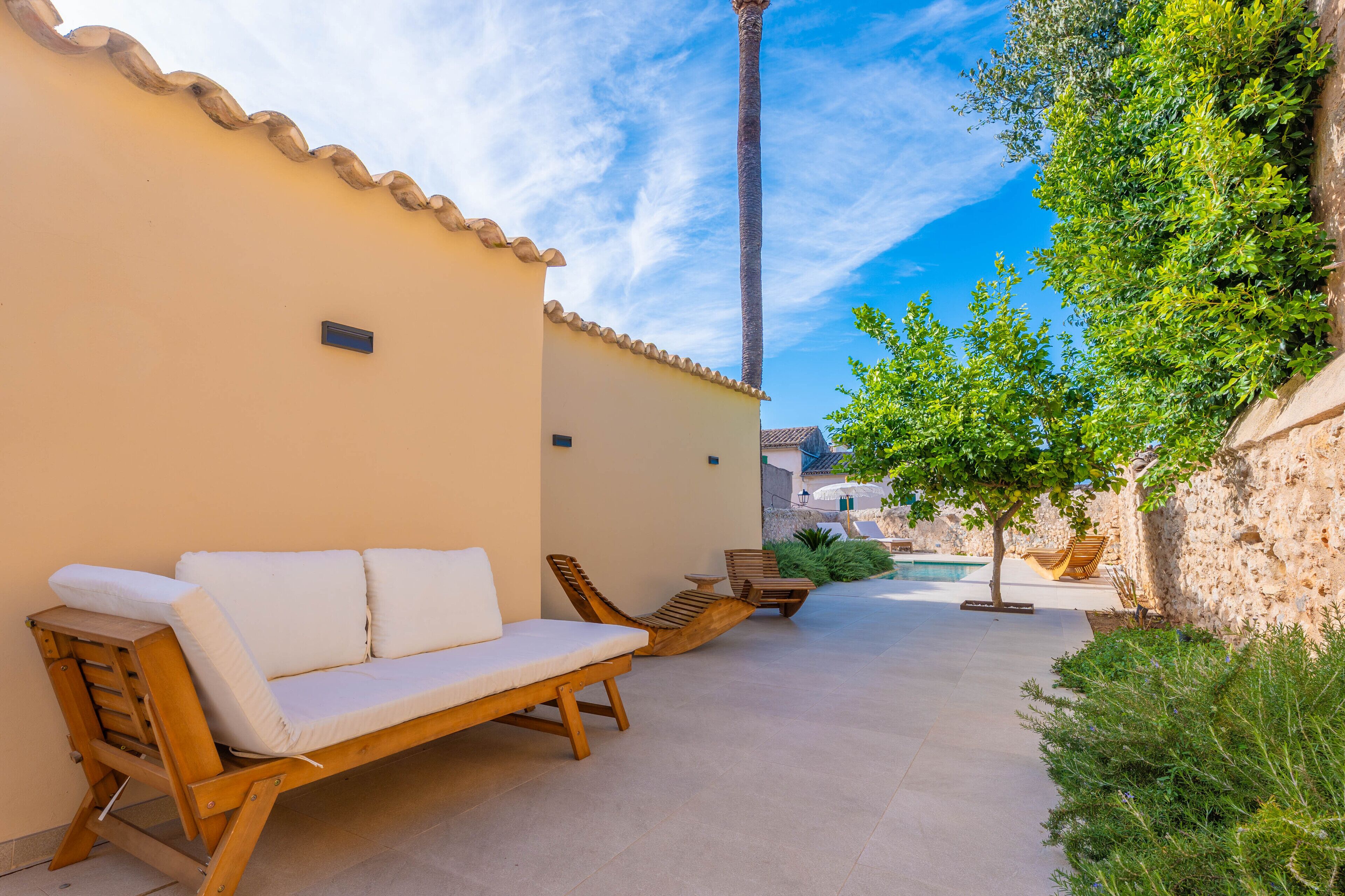A patio with a wooden sofa and lounge chairs, a small pool, and a stone wall.