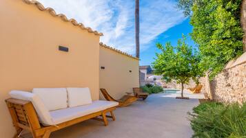 A patio with a wooden sofa and lounge chairs, a small pool, and a stone wall.