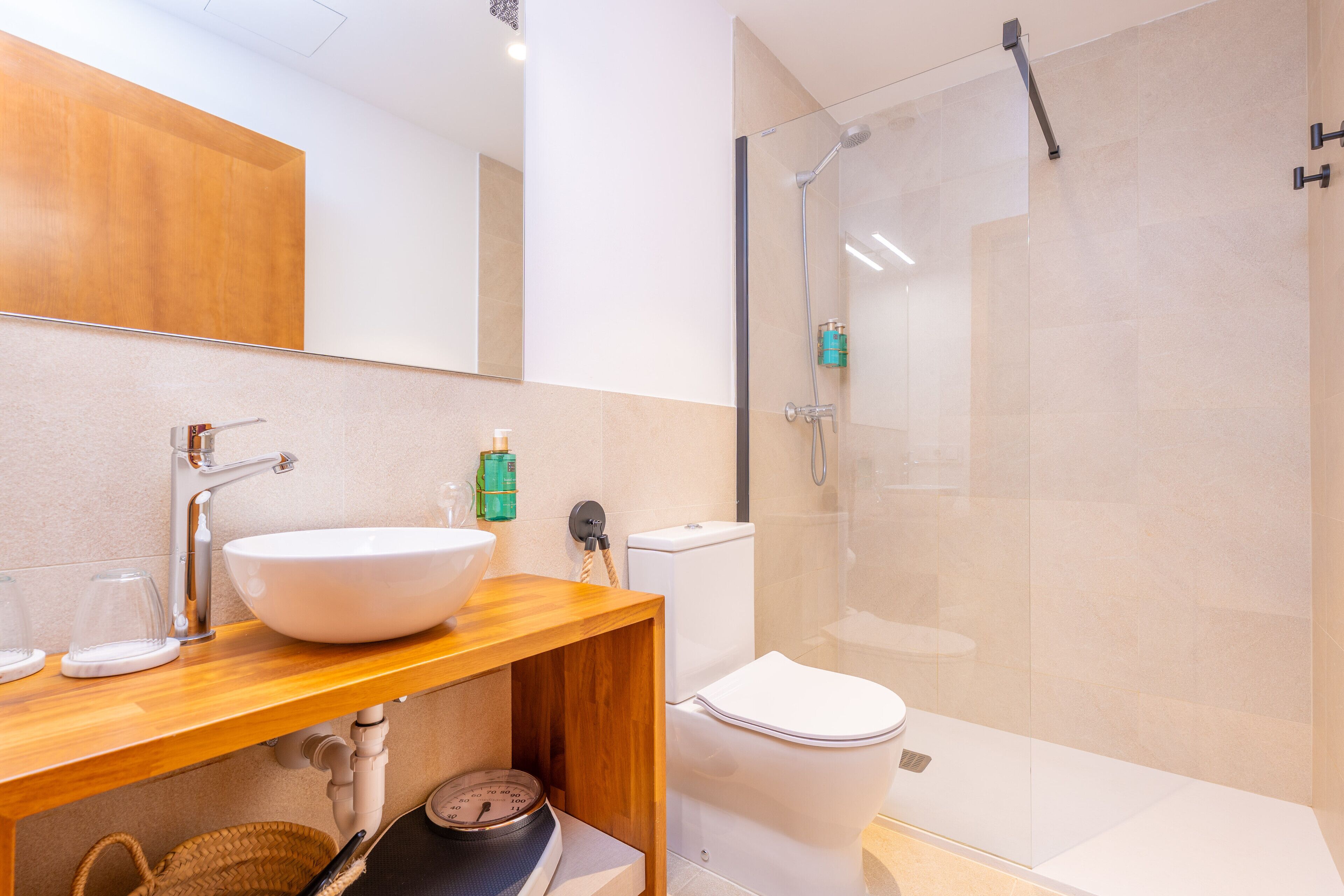 Un baño moderno con tocador de madera, lavamanos blanco, cabina de ducha de vidrio y retrete blanco.
