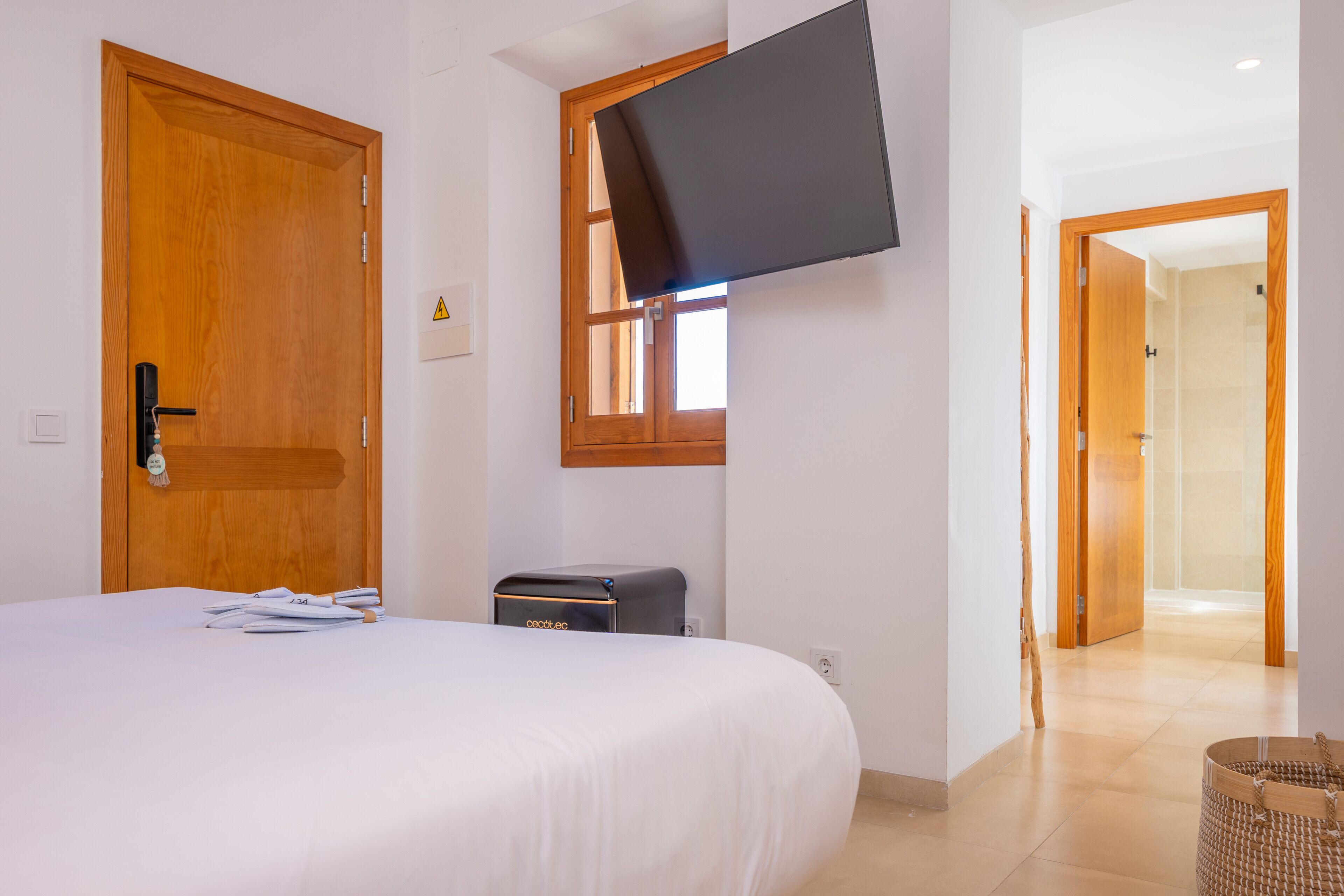 Habitación de hotel con una cama, un televisor de pantalla plana en la pared, una puerta de madera y una ventana.