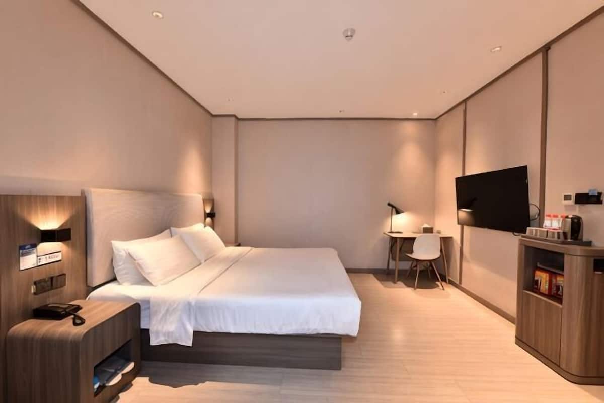 Una habitación de hotel moderna con cama, mesita de noche, televisor y un pequeño escritorio con silla.