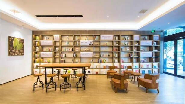 Una biblioteca moderna con estanterías de madera, una mesa larga y varias sillas.
