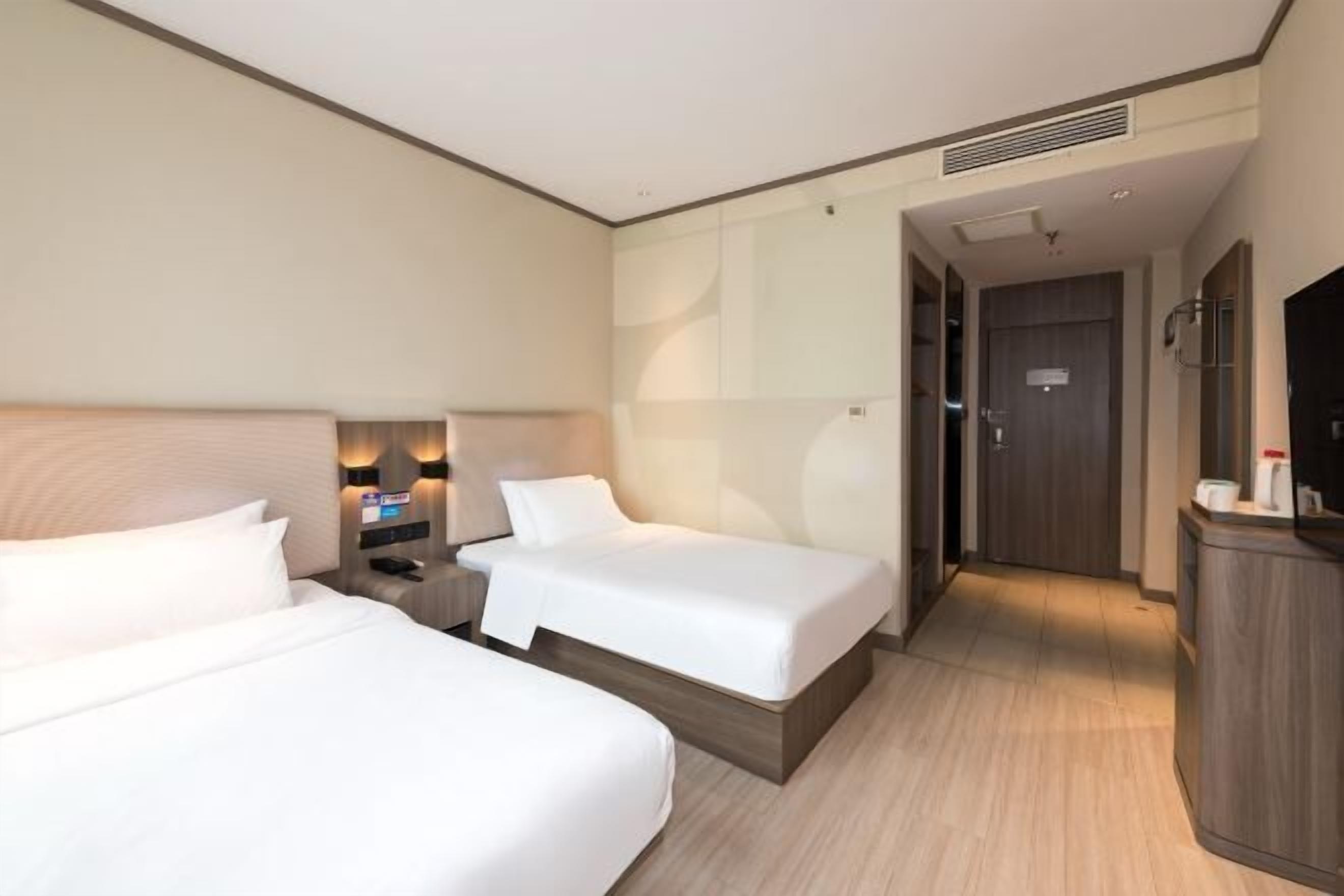 Quarto de hotel com duas camas, uma escrivaninha, televisão e porta do banheiro.