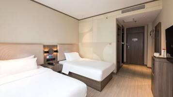 Quarto de hotel com duas camas, uma escrivaninha, televisão e porta do banheiro.