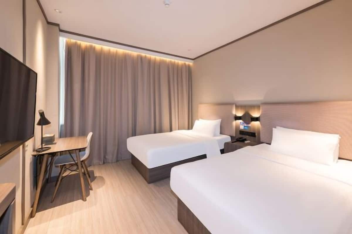 Una habitación de hotel con dos camas, un escritorio, un televisor y una ventana con cortinas.