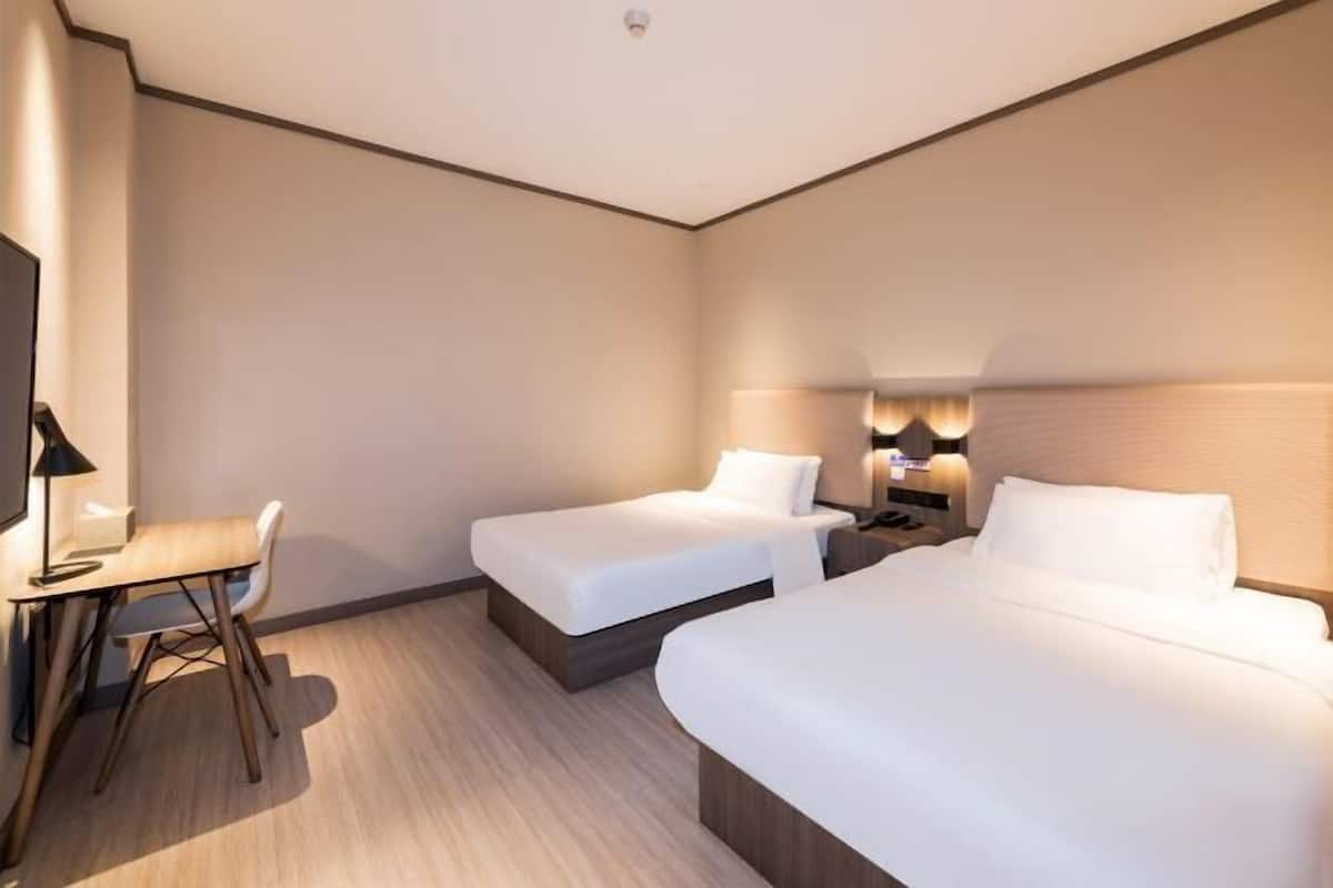 Habitación de hotel con dos camas, un escritorio, una silla y un televisor.