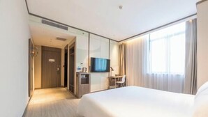 Habitación de hotel con cama, televisor, escritorio y baño visible a través de una pared de vidrio.