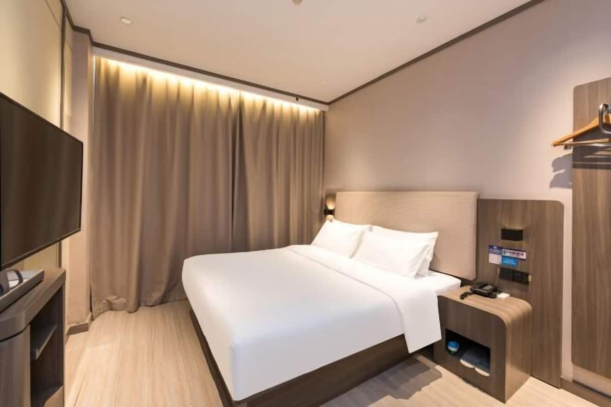 Una habitación de hotel moderna con una cama grande, un televisor de pantalla plana, una mesita de noche de madera y un armario empotrado.