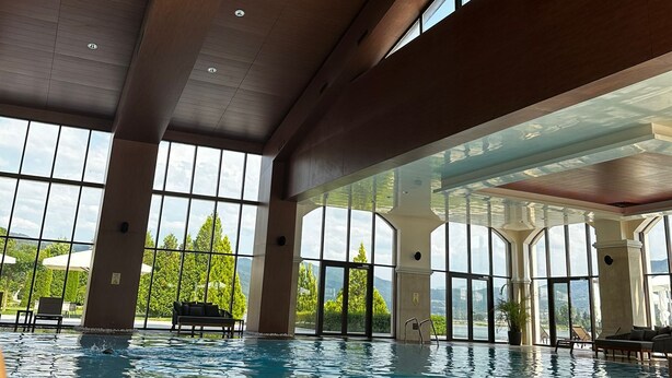 Una piscina interior con amplias ventanas, techo de madera y sillones de descanso.