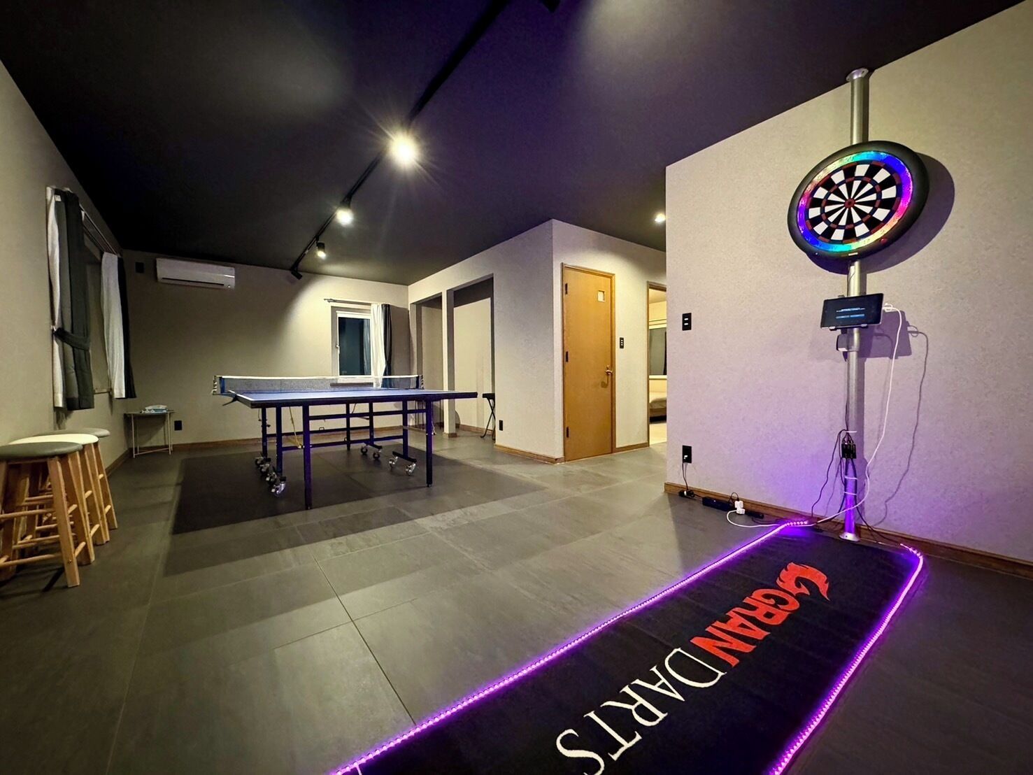 A room with a ping pong table, dartboard, and a carpet with 'GAMING' written on it.