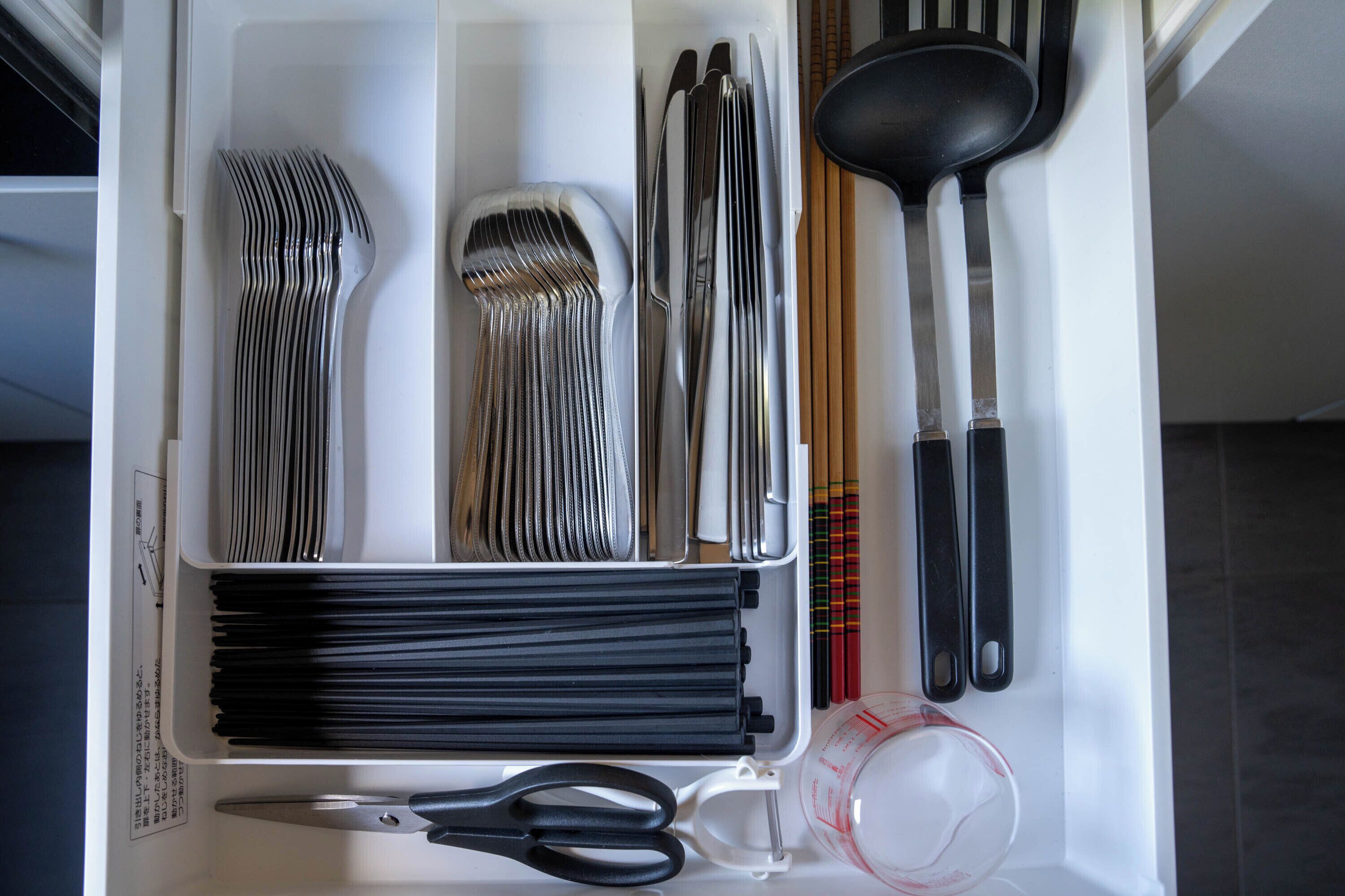 A drawer containing various kitchen utensils including forks, knives, and a measuring cup.