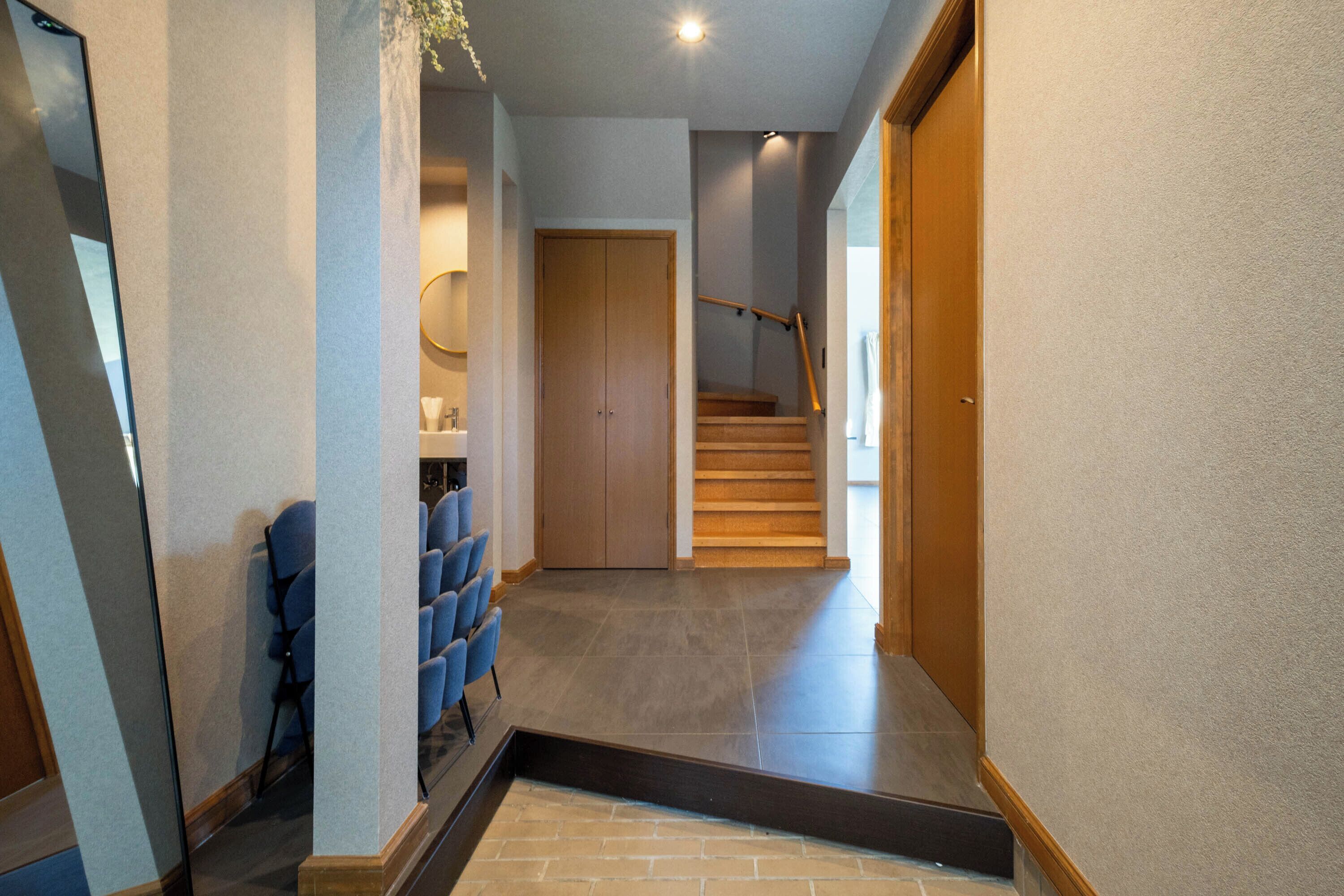 A hallway with a staircase, a seating area with chairs, and a wooden door.