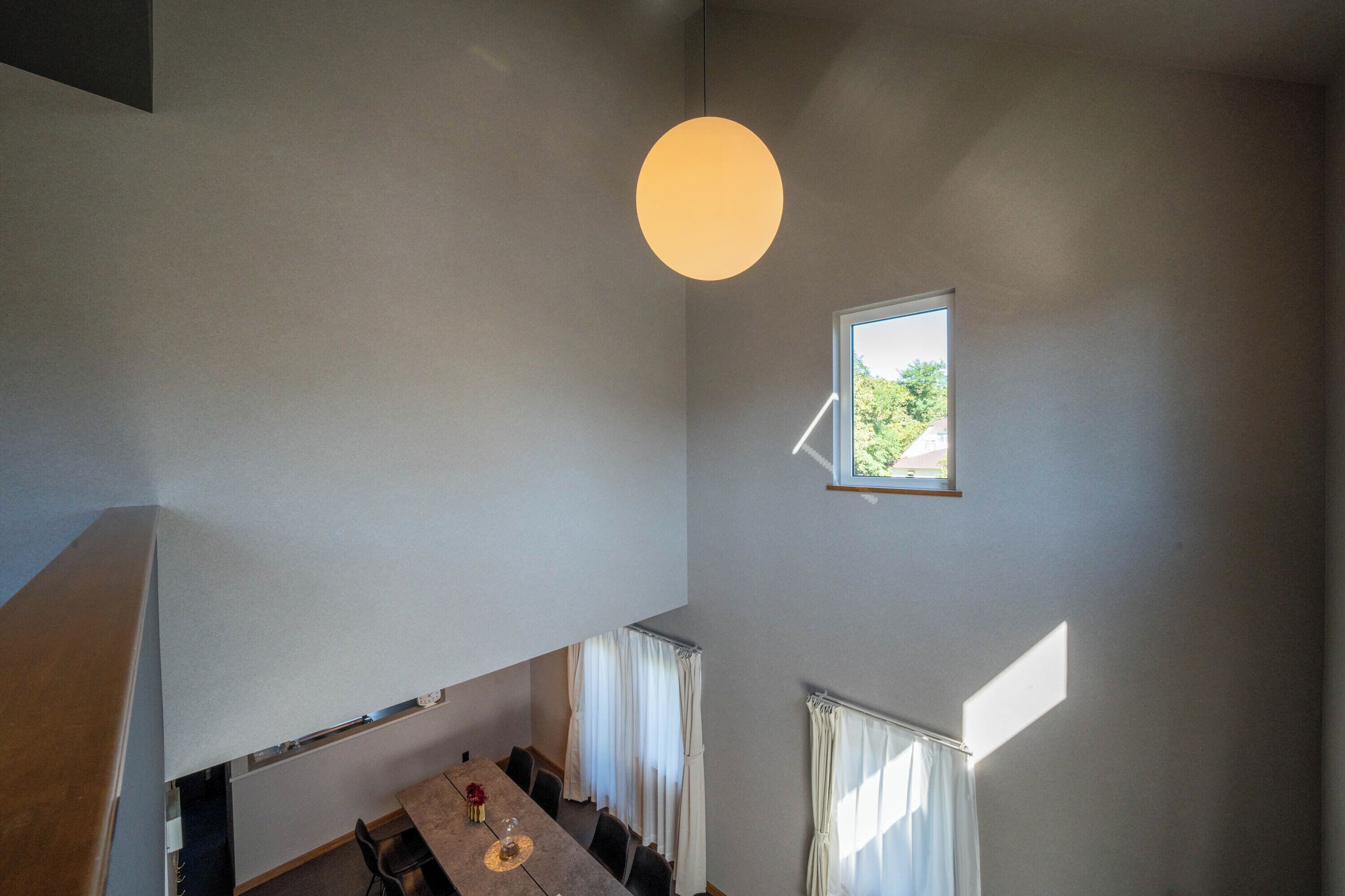 A dining area with a table and chairs, a hanging light fixture, and a window with curtains.