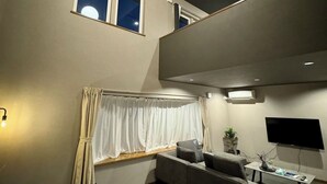 Ein modernes Wohnzimmer mit grauem Sofa, einem Flachbildfernseher und einer Deckenleuchte.