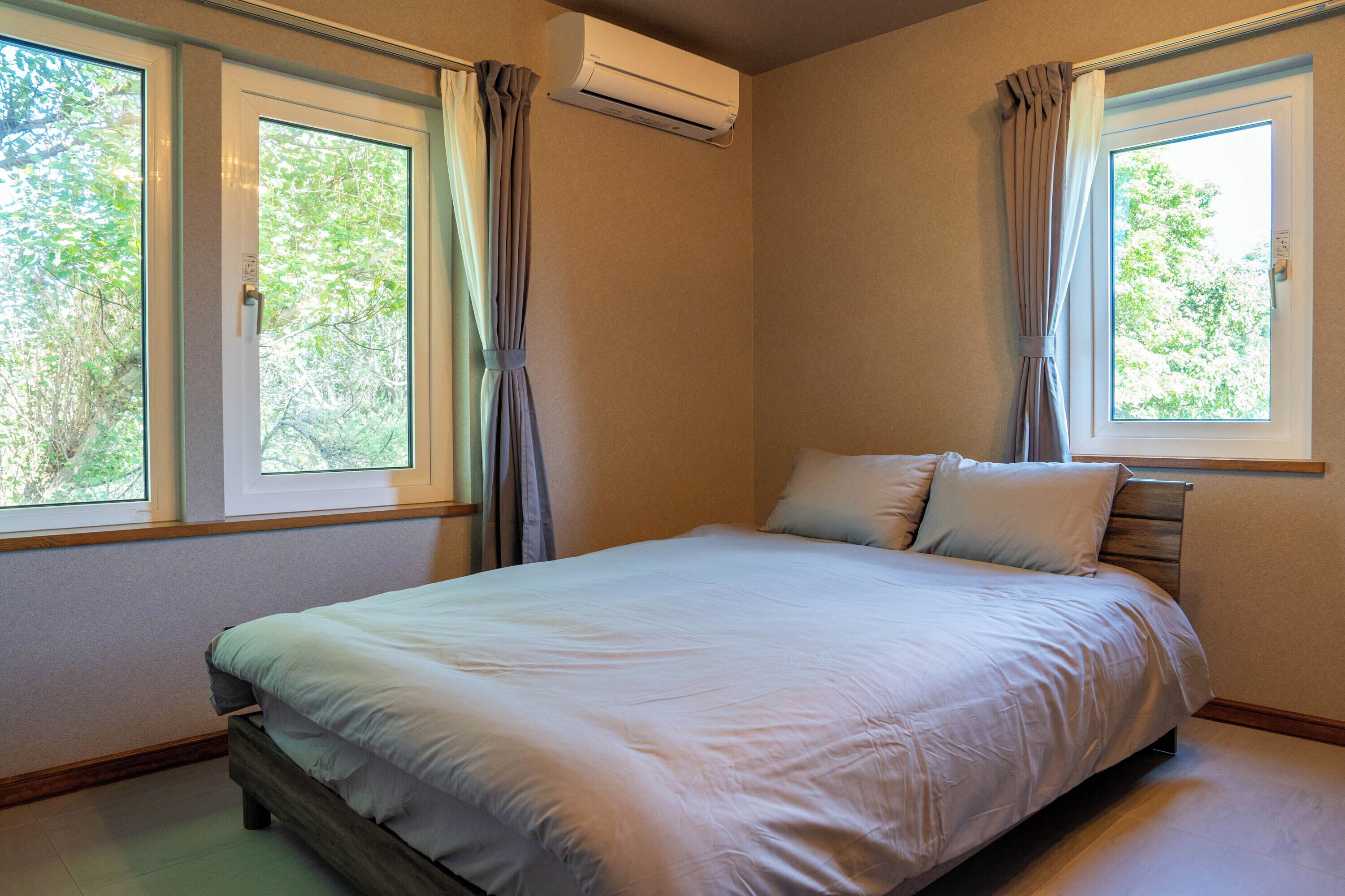 A bedroom with a bed, two windows, and an air conditioning unit.