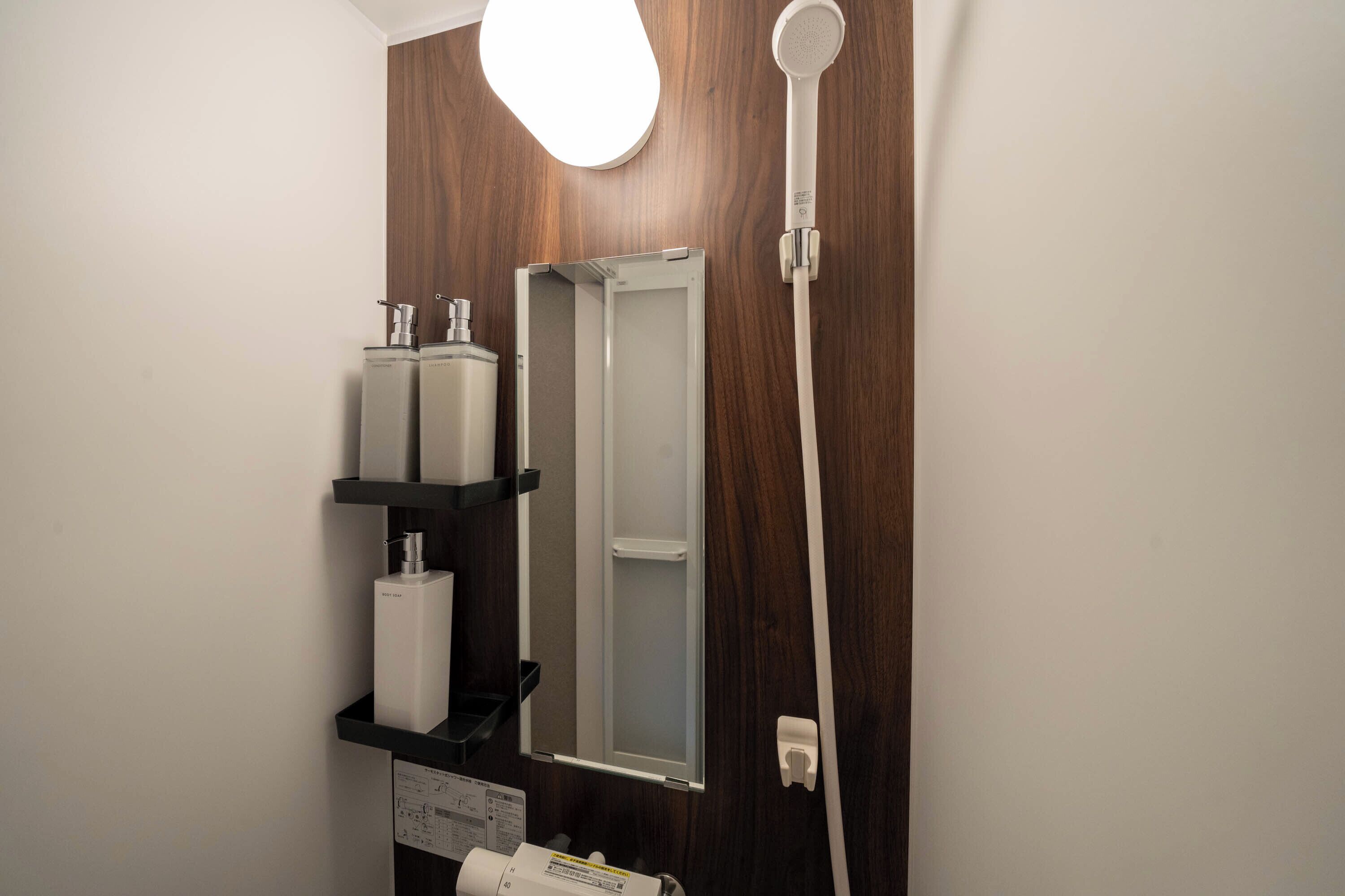 Un baño con pared de madera, ducha blanca, espejo y lavabo con dispensador de jabón.