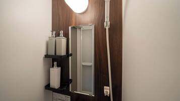 Un baño con pared de madera, ducha blanca, espejo y lavabo con dispensador de jabón.