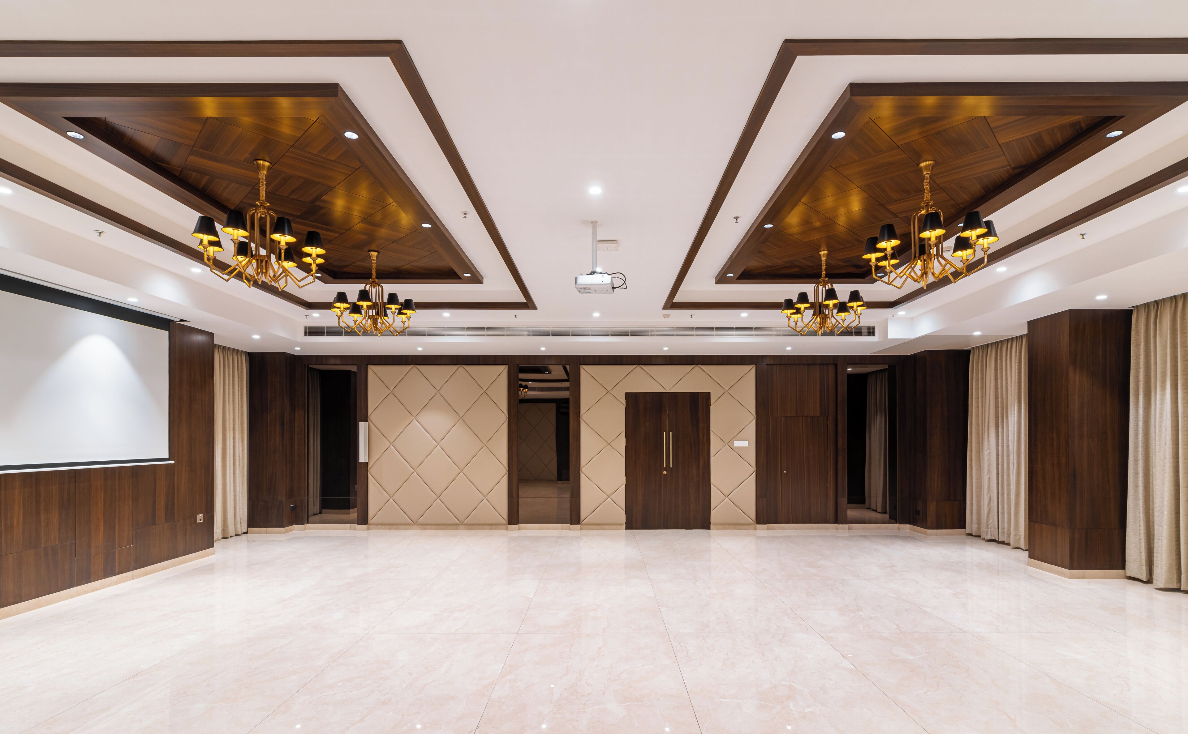 A spacious conference room with a large screen, wooden paneling, and chandeliers.