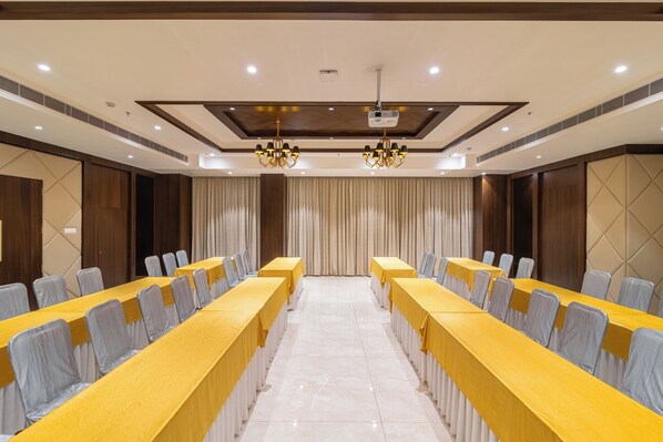 A conference room with long tables, chairs, and a projector screen. - Hotel Royal Embassy (Erode)