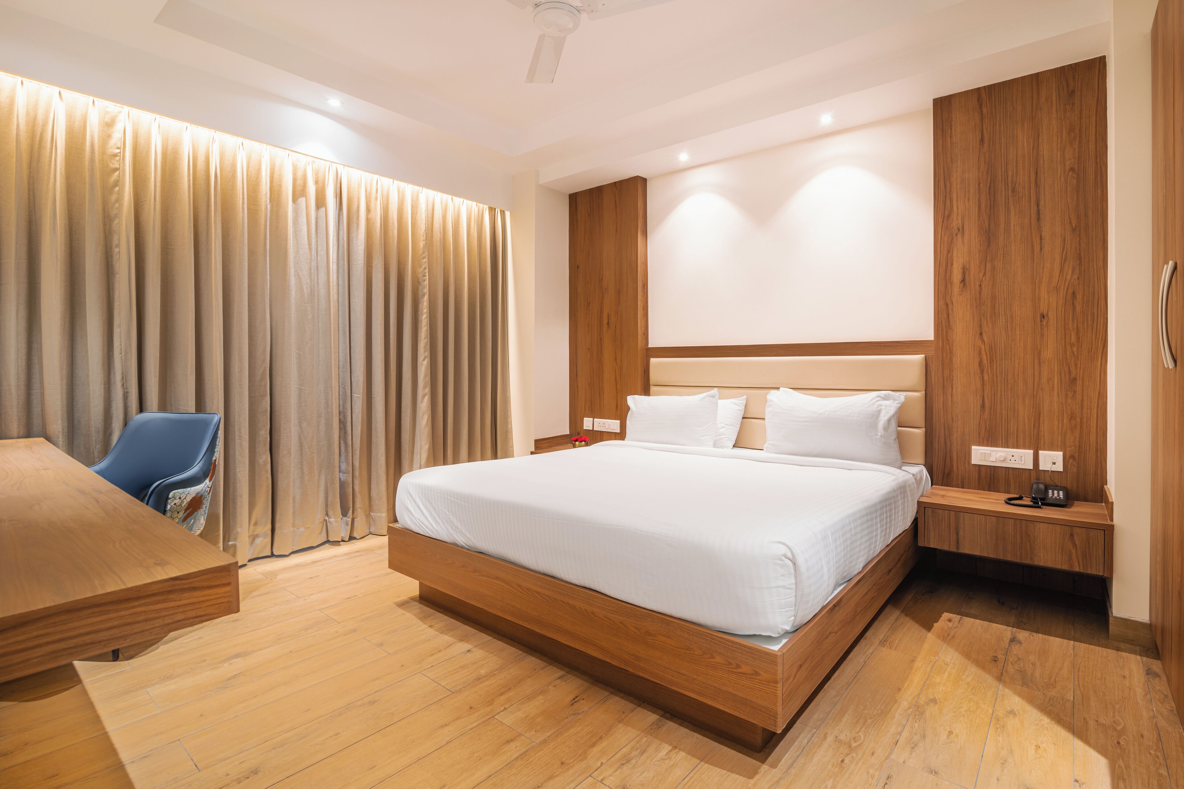 A modern hotel room with a large bed, wooden headboard, and a desk with a chair.