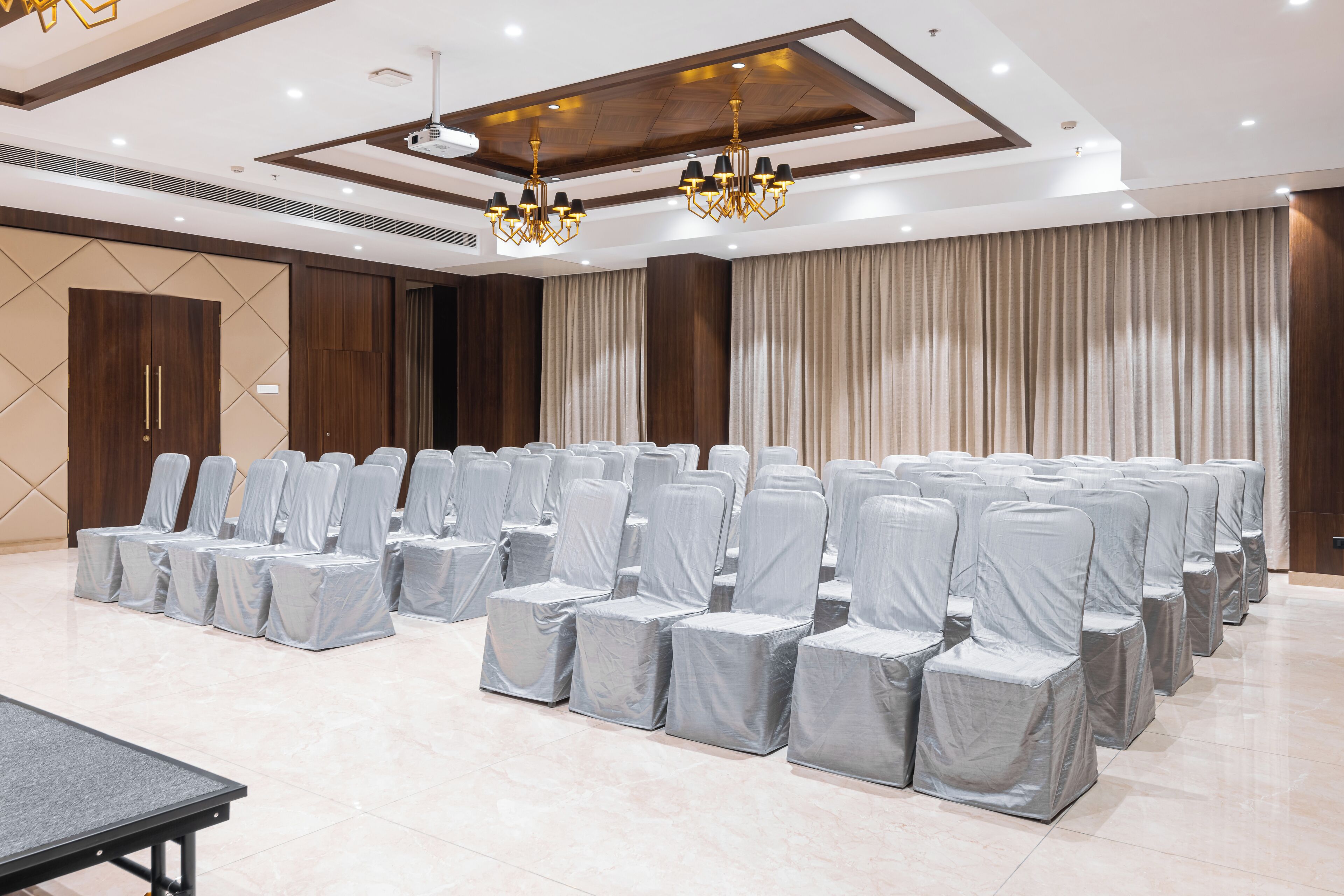 Un salón de conferencias con filas de sillas cubiertas con fundas plateadas, una mesa grande y un candelabro.