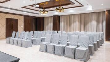 Un salón de conferencias con filas de sillas cubiertas con fundas plateadas, una mesa grande y un candelabro.