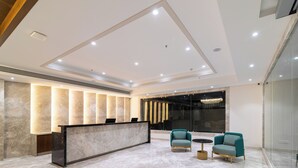 A modern reception area with a marble reception desk, two patterned armchairs, and a large window with a view of the city. - Hotel Royal Embassy (Erode)