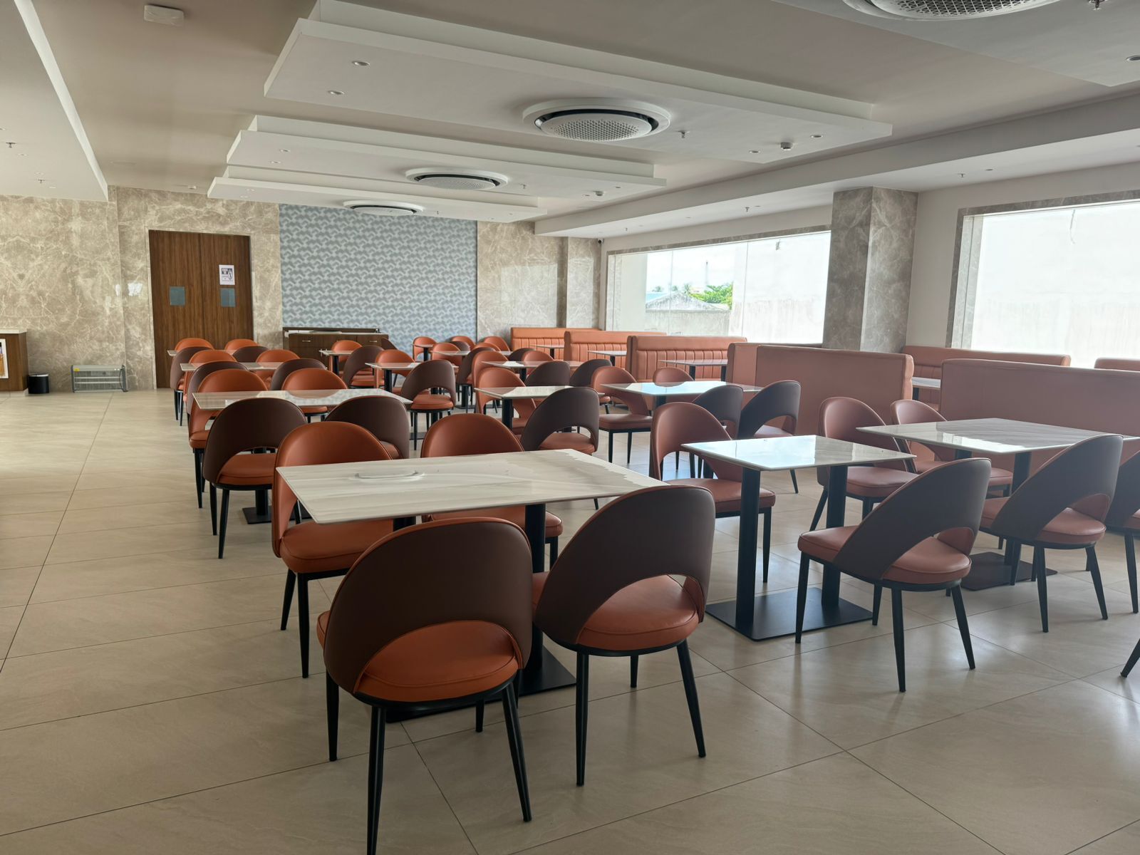 A spacious dining area with multiple tables and chairs, large windows, and a modern ceiling design.