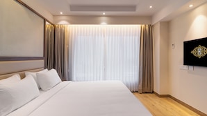 A hotel room with a large bed, a flat-screen TV mounted on the wall, and a window with curtains. - Hotel Royal Embassy (Erode)