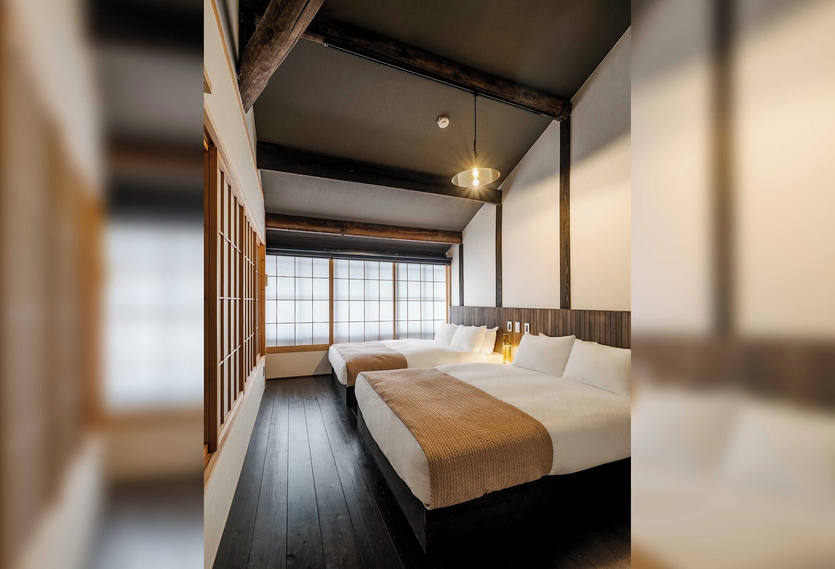 A hotel room with two beds, a wooden floor, a large window, and a hanging light fixture.