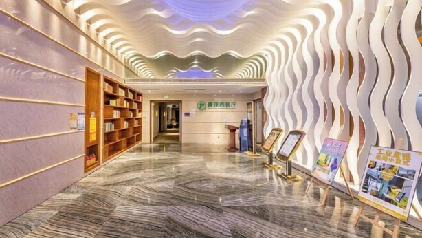 A modern hotel lobby with a marble floor, wooden bookshelves, a reception desk, and a unique wavy ceiling design. - Pengke Hotel (Shenzhen North Railway Station Shangmu) (Shenzhen)