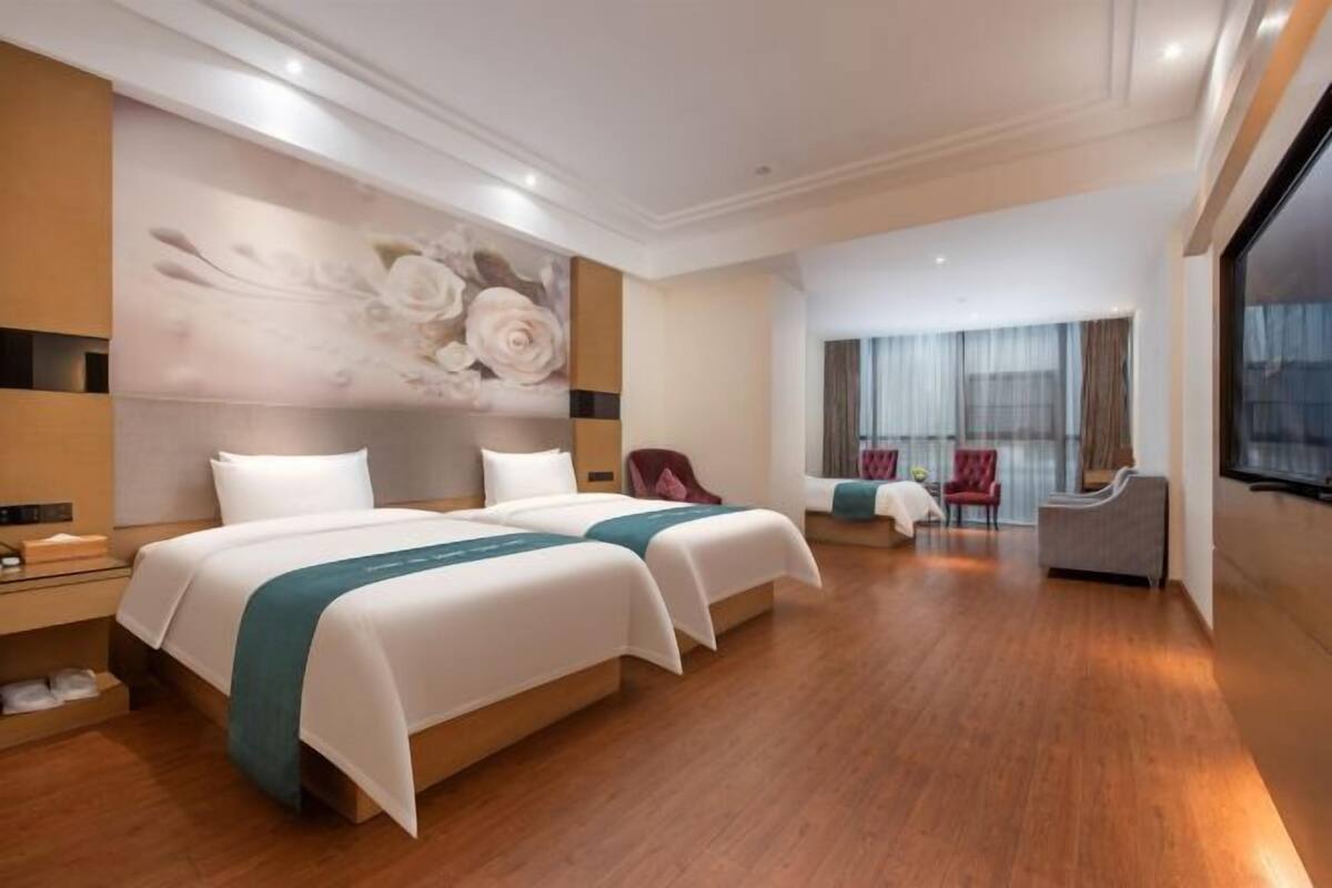 A hotel room with two beds, a large window, a seating area with chairs, and a wall with a floral mural.