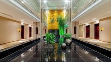 A hotel corridor with a reflective black floor, a central plant, and doors on either side.