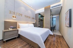 A modern hotel room with a bed, bedside table, and a wall with the text 'ENJOY YOUR LIFE'.