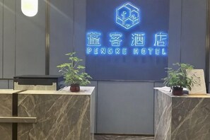A reception desk with a neon sign for Pengke Hotel, two potted plants, and a framed picture on the counter.