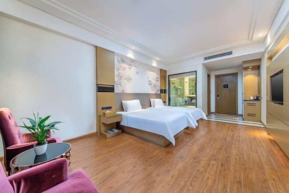A hotel room with a large bed, a desk, a chair, and a potted plant.
