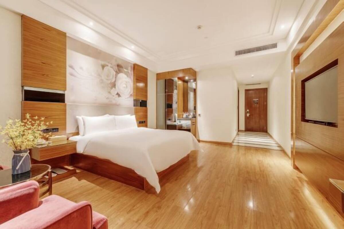 A hotel room with a large bed, wooden paneling, a flat-screen TV, and a small table with a vase of flowers.
