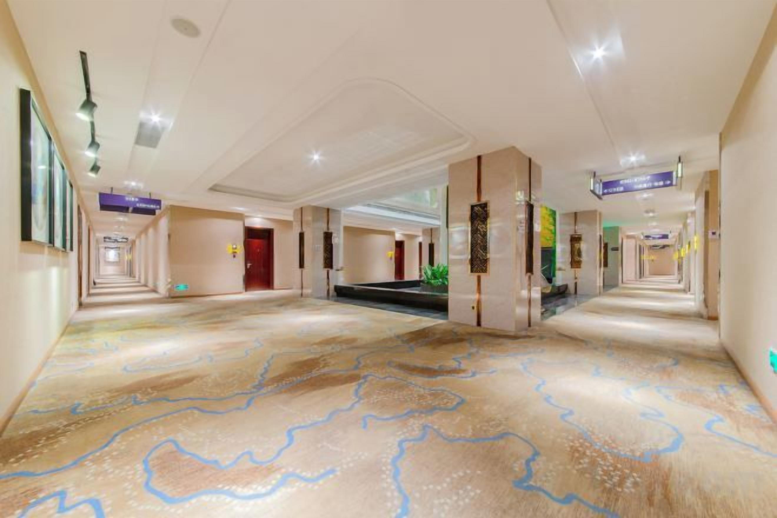 A hotel corridor with a patterned carpet, directional signs, and a staircase leading to another level.