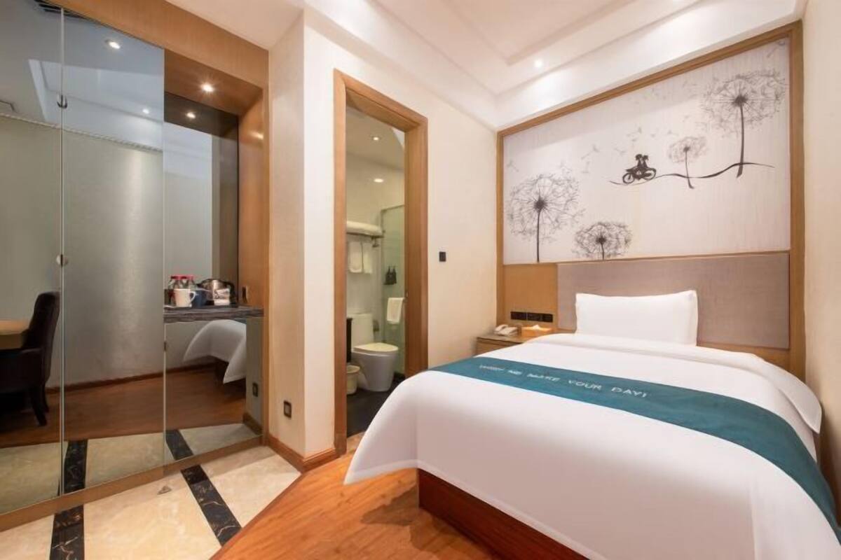 A hotel room with a bed, a desk, a mirror, and a bathroom visible through an open door.