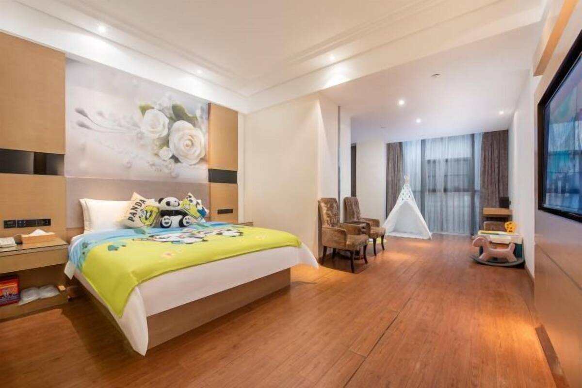 A hotel room with a bed, a chair, a small table, a window, and a wall with a floral design.
