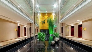A modern hotel lobby with a reflective black floor, a central green plant, and a yellow wall with a decorative pattern. - Pengke Hotel (Shenzhen North Railway Station Shangmu) (Shenzhen)