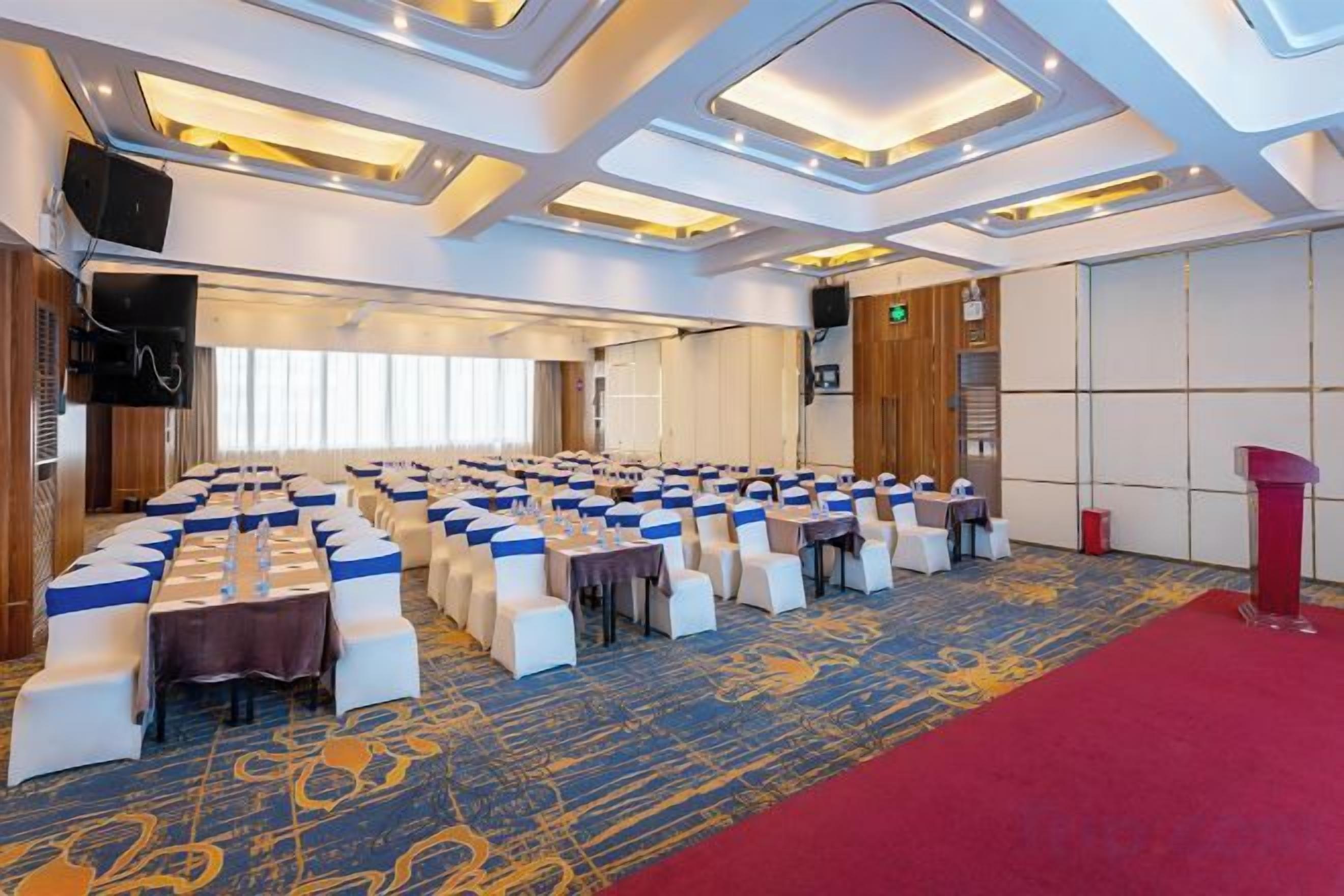 A conference room with rows of tables and chairs, a red carpet, and a stage with a podium.
